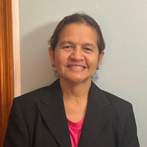 Retrato de Olga León, escritora venezolana y exprofesora de idiomas, sonriendo, vestida con chaqueta negra y camiseta fucsia, frente a una pared clara.